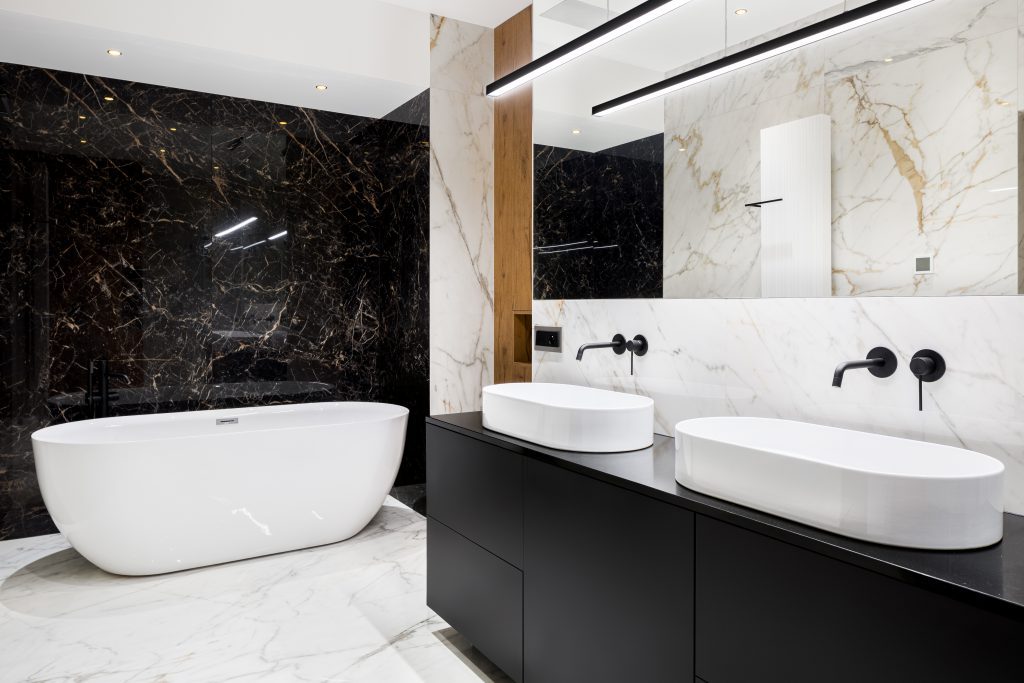 Luxury bathroom with black and white marble tiles on walls and floor and big, oval bathtub