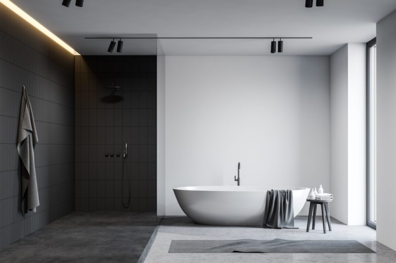 Interior of spacious loft bathroom with white and grey tiled walls, comfortable bathtub and shower stall with glass wall.